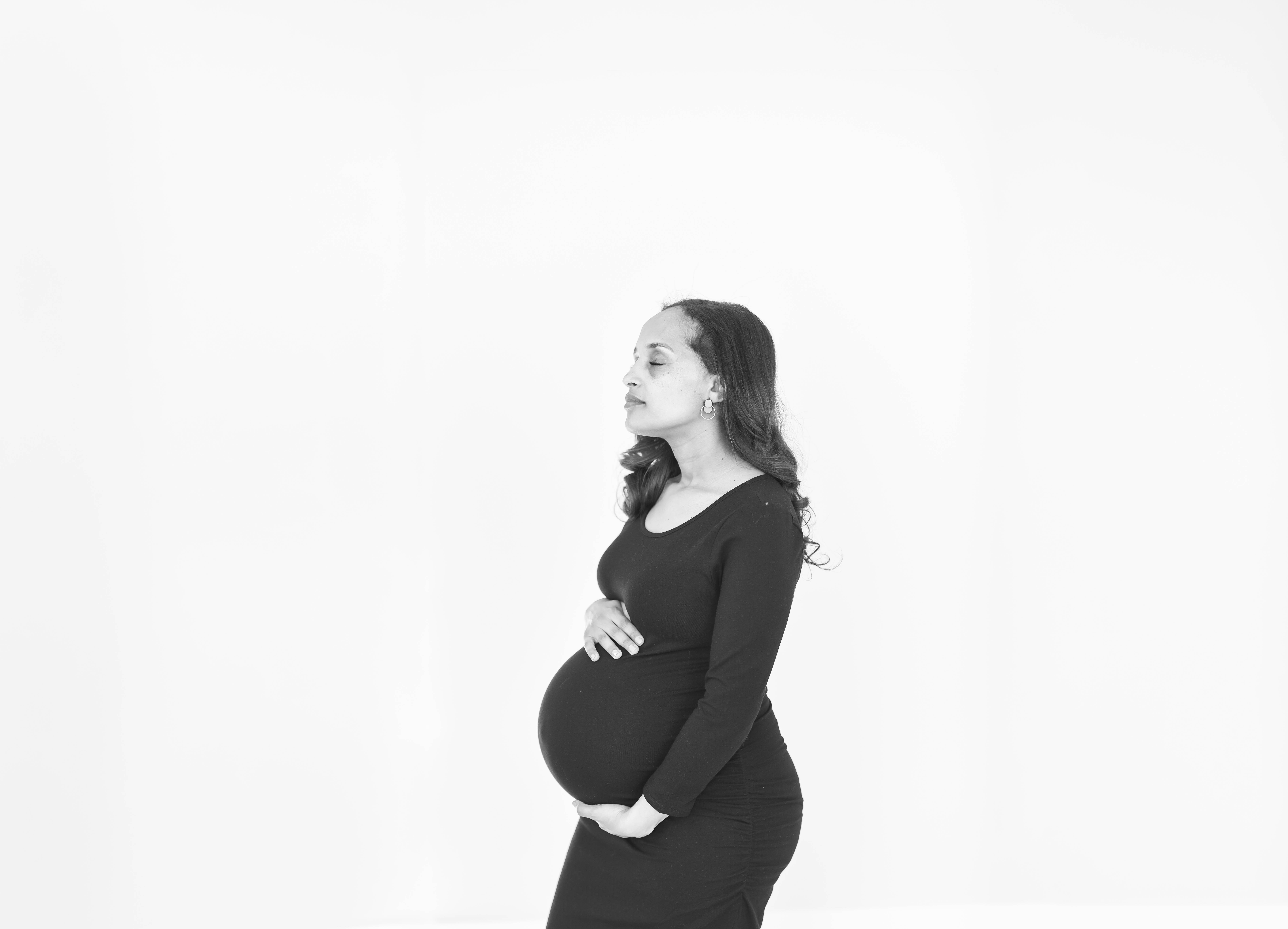 denver maternity photographer- a pregnant women stands next to a white wall