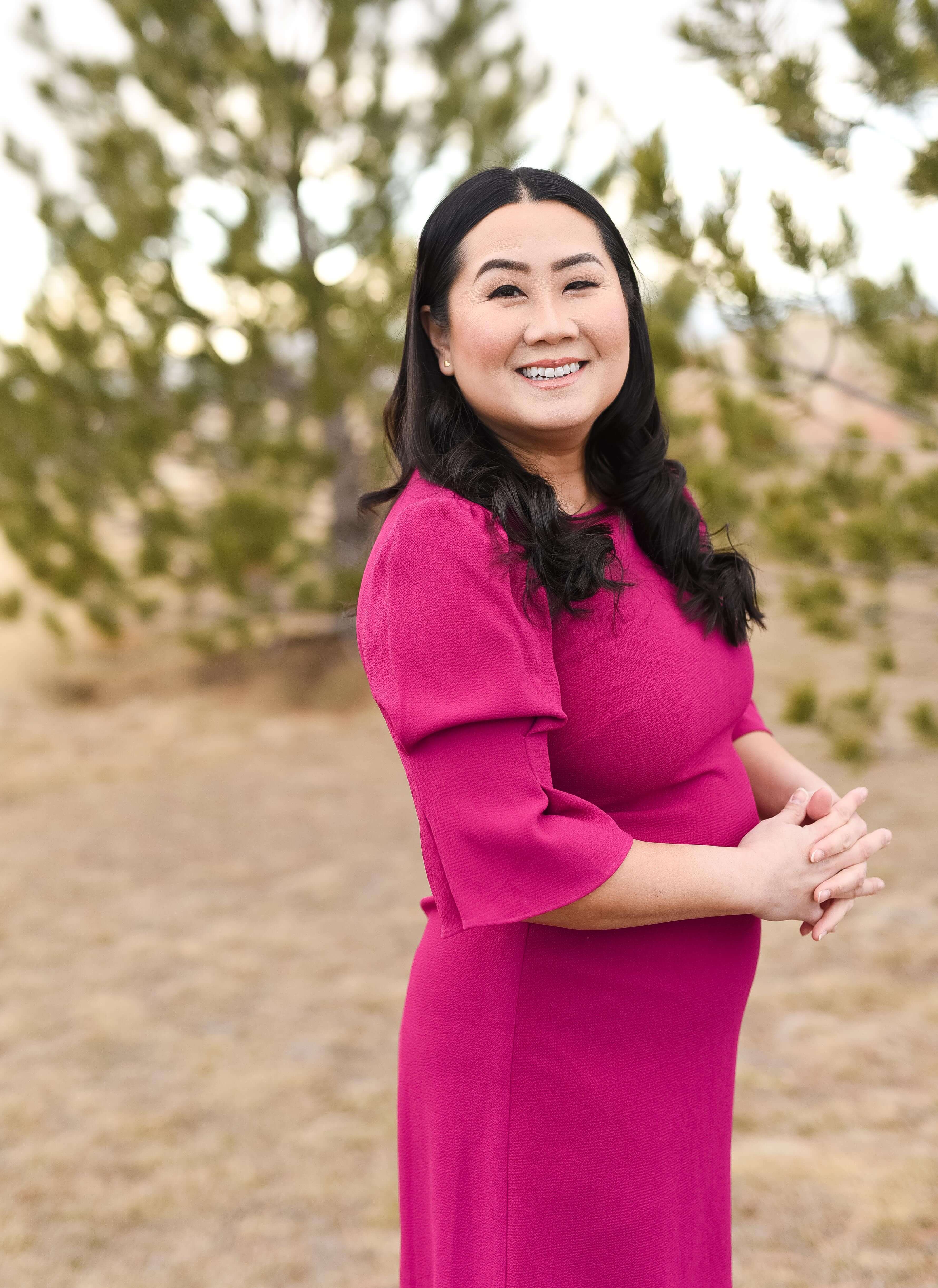 a women stands among evergreen trees, posing in a pink dress