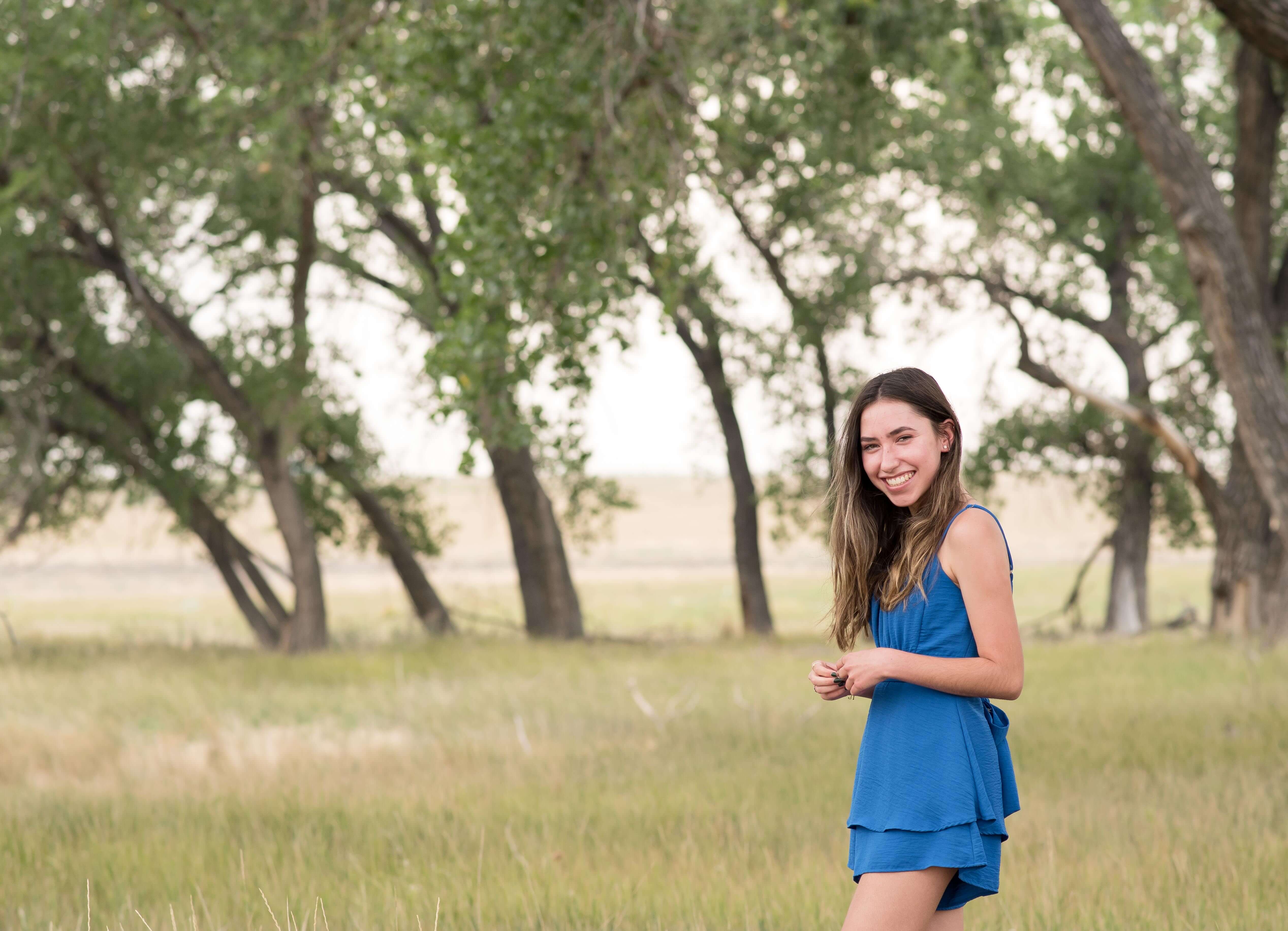 a denver senior poses in a green field under trees at rocky mountain arsenal