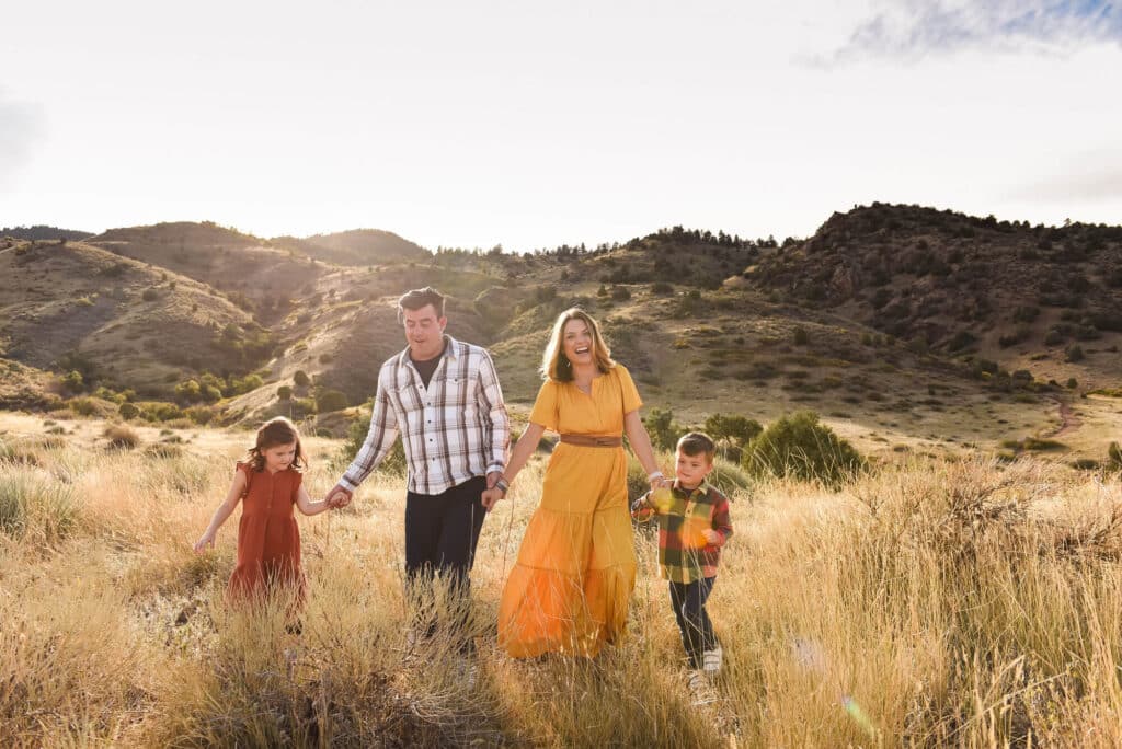 a family of four walks through a golden field at sunset in the Denver flatirons
