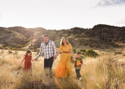 a family of four walks through a golden field at sunset in the Denver flatirons