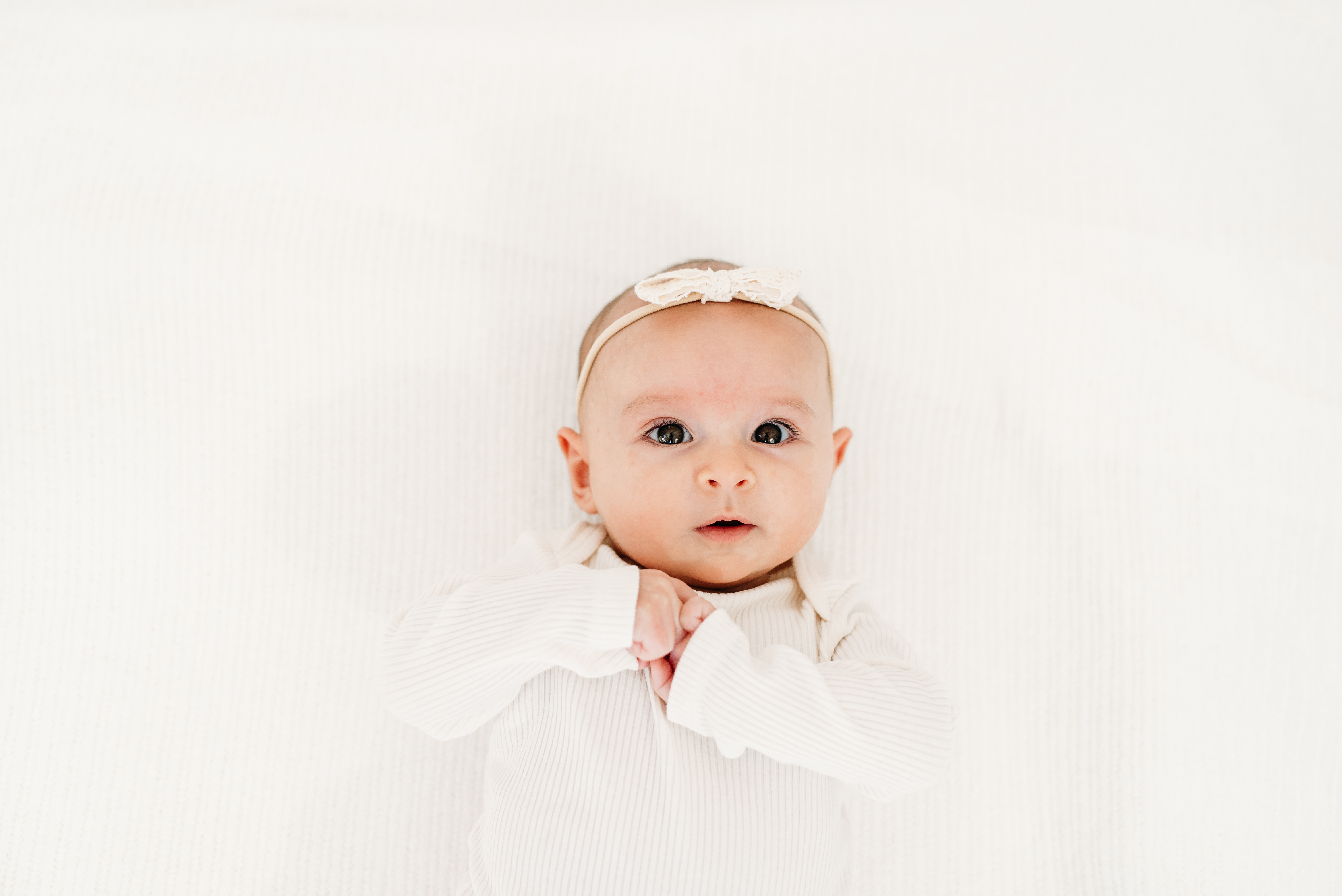 a wide-awake 3 month old rests on a white blanket