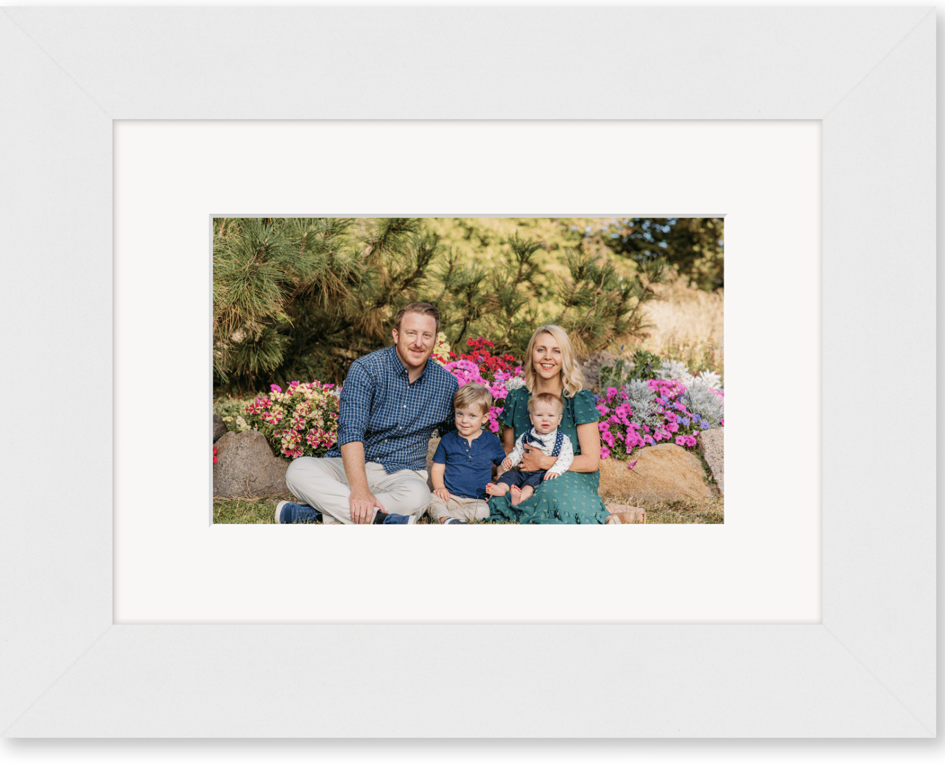 an image of a family of four sits in a garden and the picture is  in a white frame 