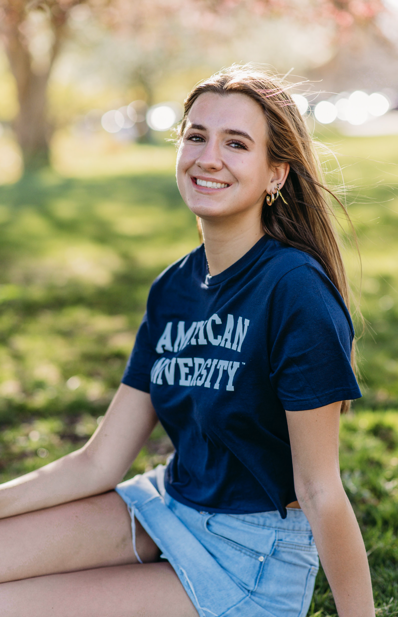 a senior poses under a flowering tree wearing a college shirt